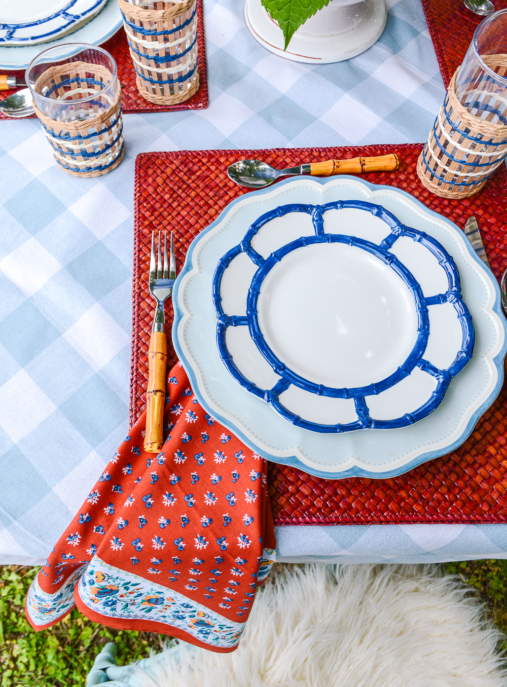 Blue bamboo melamine salad plates with Lenox Provencal dinner plates on top of a red woven placemat and blue gingham tablecloth