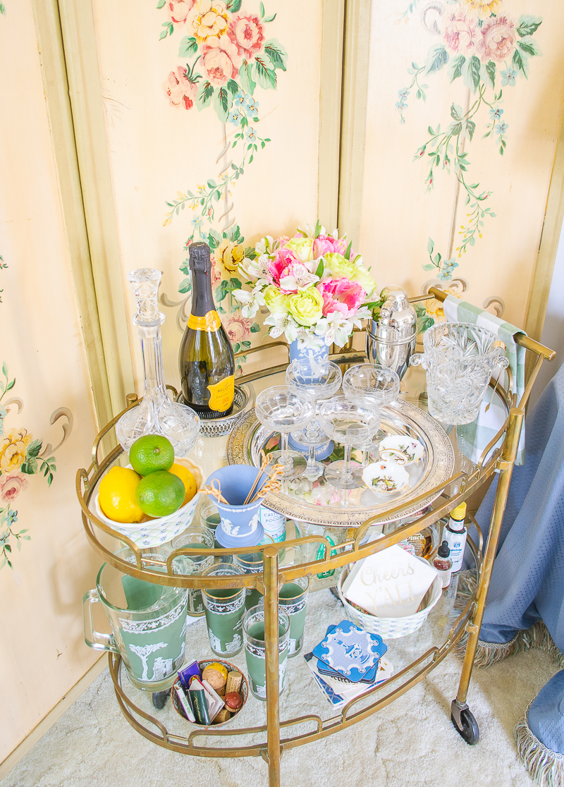 A vintage brass barcart shows the art of layering with a mix of crystal, ceramics, florals, and shapes