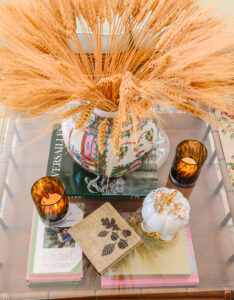 On the coffee table a rose medallion ginger jar filled with dried wheat, tortoise shell votives, and a Mottahedeh pumpkin create a pretty autumn vignette