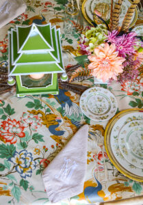 A green pagoda lantern flanked by Lenox peach urns filled with faux dahlias, asters, hydrangea, and pheasant feathers creates a charming and lush centerpiece for this Asian inspired tablescape.