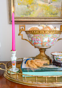 A rose medallion ormolu bowl filled with pumpkins and hot pink candles decorate a sideboard for autumn decor in the living room