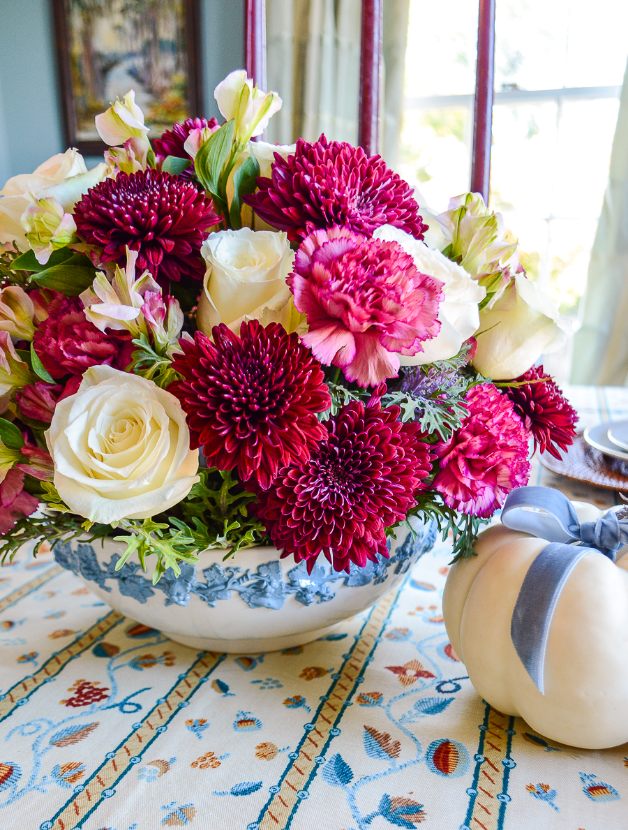 Bowl full of flowers, including deep burgundy dahlias and chrysanthemums, pink carnations, and white roses in a blue and white Wedgwood shallow bowl