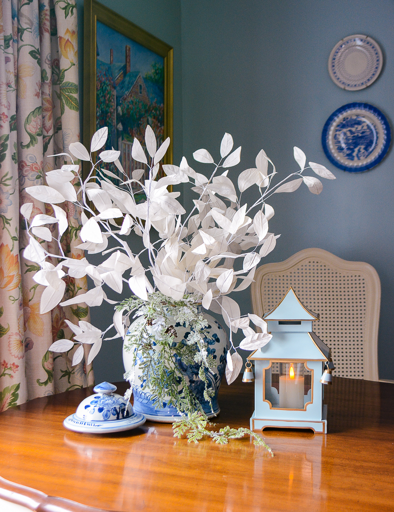 A winter floral centerpiece with frosted cedar and white paper branches fill a blue and white Chinese jar.