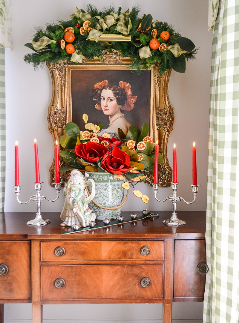 Sideboard decorated with magnolia arrangement, sleigh bells, silver candelabras, and Fitz & Floyd Santa.