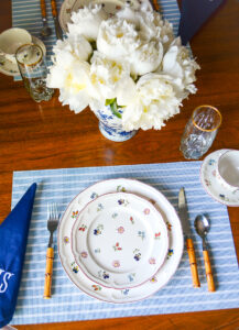Breakfast table setting with Villeroy & Boch Petite Fleur dishes, blue and white striped placemats, navy monogrammed napkins, bamboo flatware, and white peonies in Chinese jar