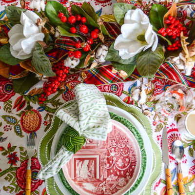 A Christmas tablescape with Wedgwood and cabbageware plates, Indian block print linens, bamboo flatware, and magnolia and red berry garland centerpiece