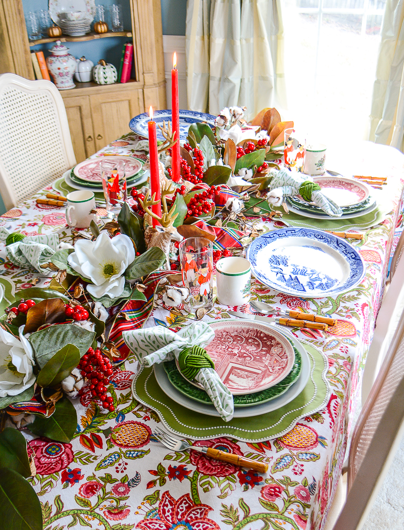 A Christmas tablescape with Wedgwood and cabbageware plates, Indian block print linens, bamboo flatware, and magnolia and red berry garland centerpiece