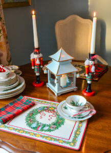 The breakfast table decorated for Christmas with 12 days of Christmas placemats, holiday china, plaid napkins, Chinese lantern, and nutcracker candleholders