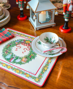 The breakfast table decorated for Christmas with 12 days of Christmas placemats, holiday china, plaid napkins, Chinese lantern, and nutcracker candleholders