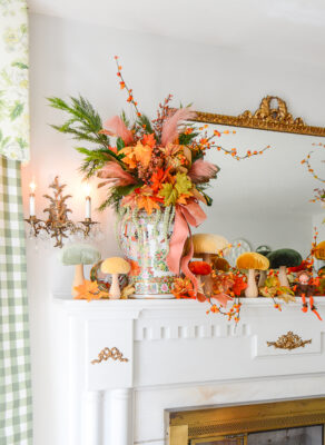 A magical autumn mantel arrangement with velvet mushrooms, Rose Medallion, fall leaves, bittersweet, and whimsical elves
