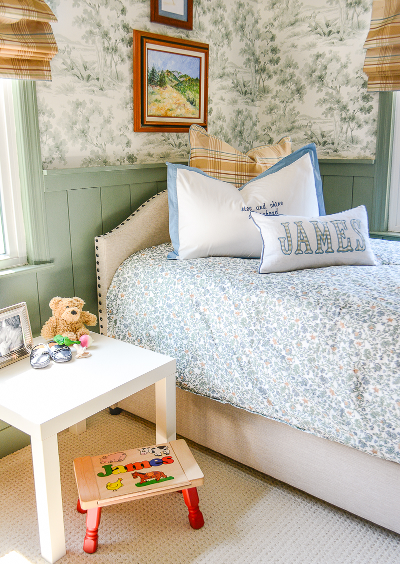 Twin bed in baby boy's nursery decorated in a woodland theme with green toile wallpaper and plaid curtains