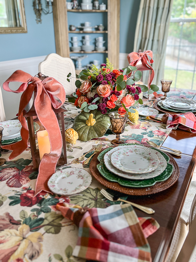 Autumn table decor with pretty floral chintz, plaid napkins, maple leaf china, and pumpkin floral centerpiece