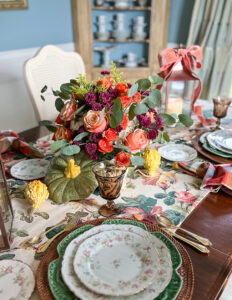 Autumn table decor with pretty floral chintz, plaid napkins, maple leaf china, and pumpkin floral centerpiece