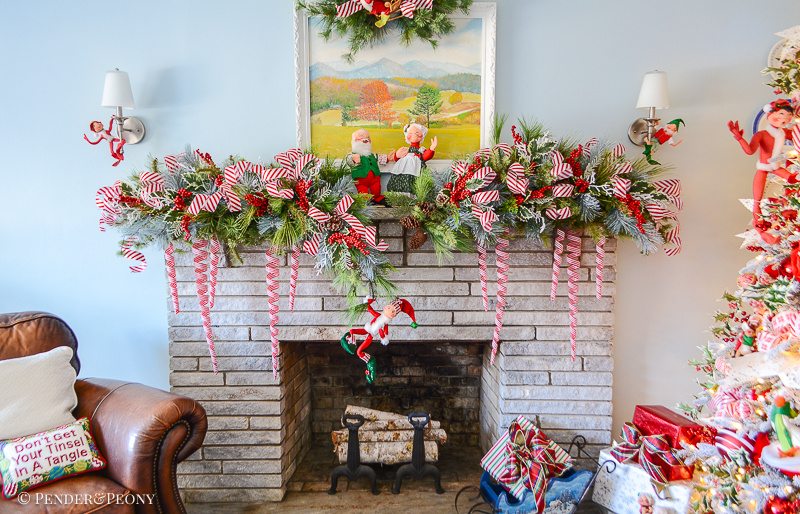 Stone mantel decorated with pine garland and candy cane stripe red and white ribbon. Annalee elves swing from the branches