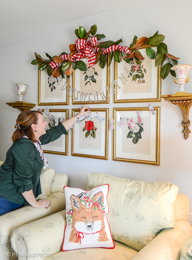 Katherine tapes up "12 Days of Christmas" banner on camellia botanical gallery wall