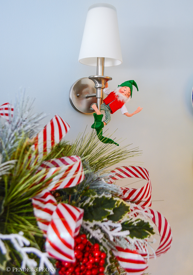 Annalee elf swings from light sconce above mantel