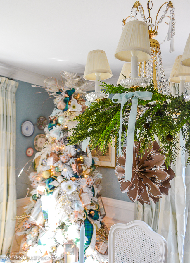 Crystal chandelier decorated with cedar branches, blue velvet bows, and a paper snowflake