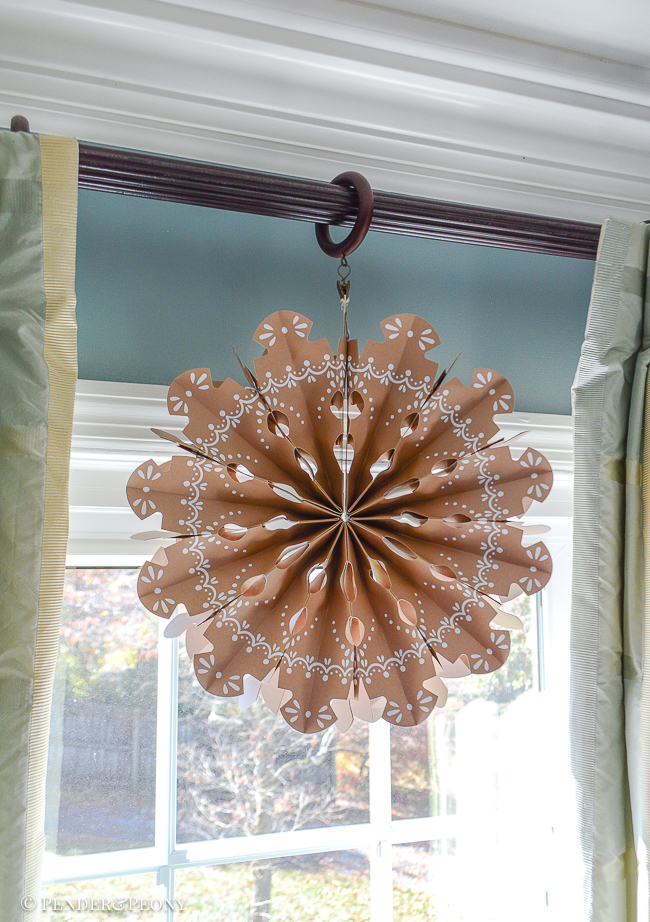 Large paper snowflake hangs from curtain rod in front of window