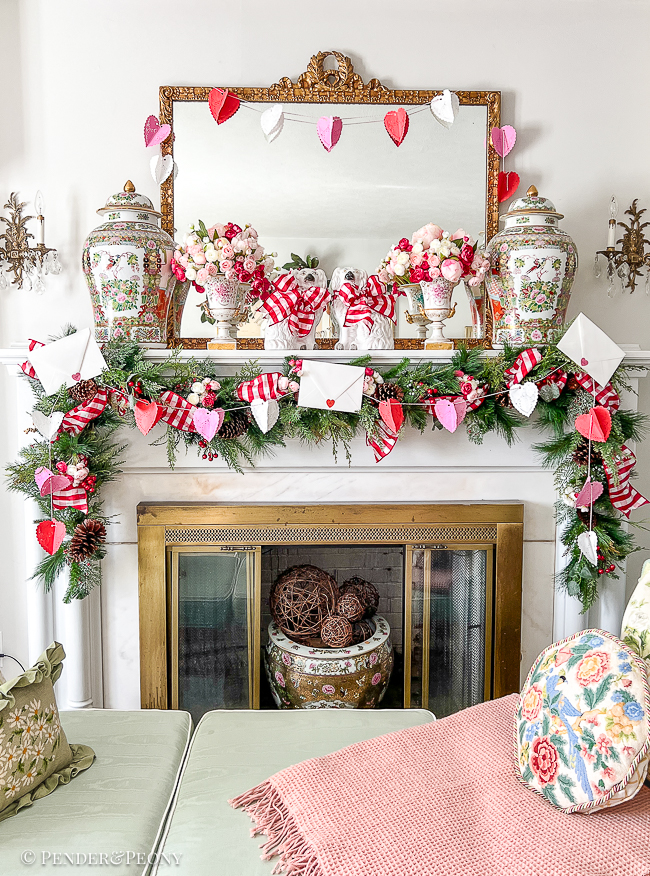 A red and pink Valentine's Day mantel with crafted paper heart doily garland, gingham ribbon, love letters, and blooms