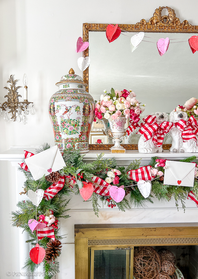 A red and pink Valentine's Day mantel with crafted paper heart doily garland, gingham ribbon, love letters, and blooms