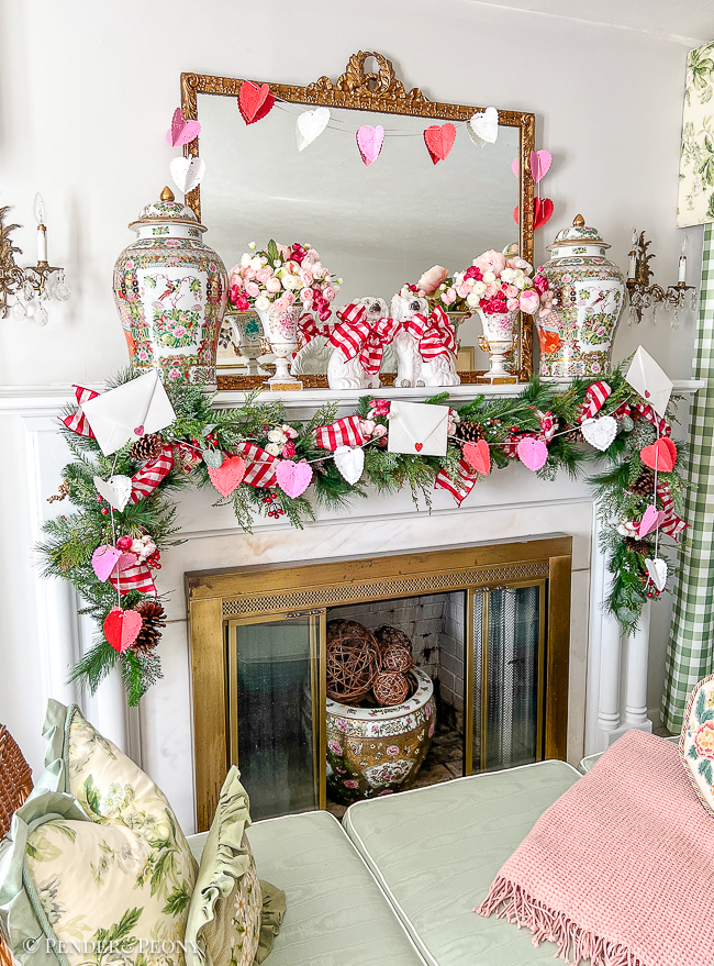A red and pink Valentine's Day mantel with crafted paper heart doily garland, gingham ribbon, love letters, and blooms