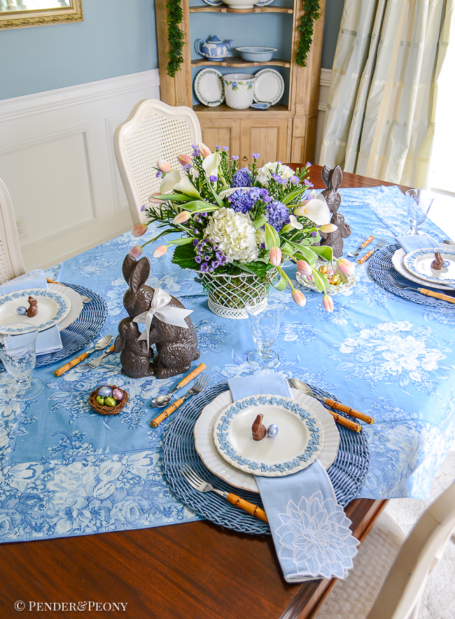 An Easter table in blue and white with Wedgwood Queen's Ware, chocolate bunnies, French wire basket filled with flowers, and April Cornell chintz tablecloth.