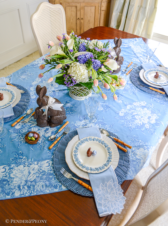 An Easter table in blue and white with Wedgwood Queen's Ware, chocolate bunnies, French wire basket filled with flowers, and April Cornell chintz tablecloth.