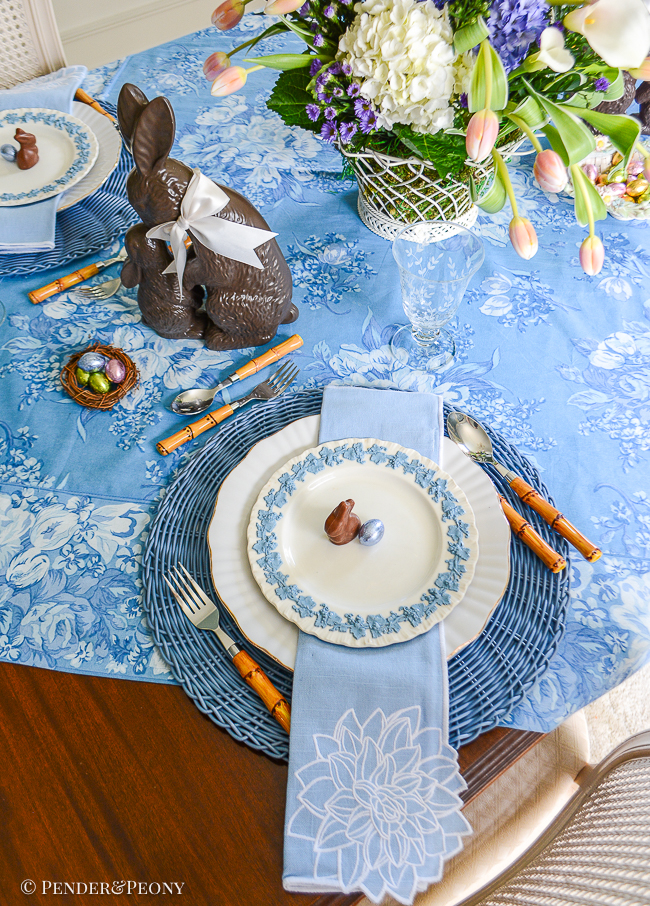 An Easter table in blue and white with Wedgwood Queen's Ware, chocolate bunnies, French wire basket filled with flowers, and April Cornell chintz tablecloth.