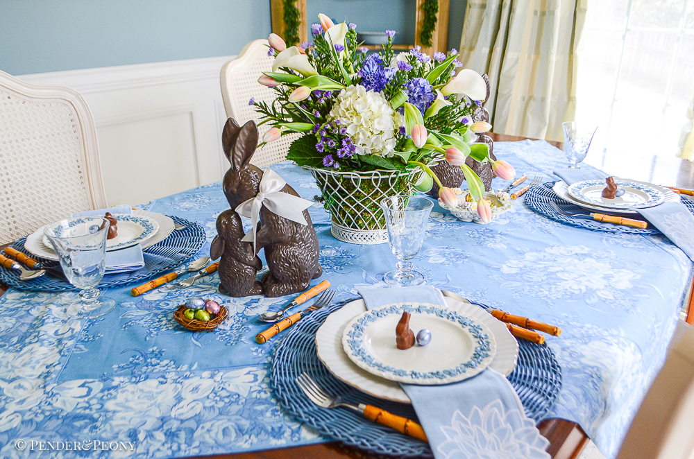 An Easter table in blue and white with Wedgwood Queen's Ware, chocolate bunnies, French wire basket filled with flowers, and April Cornell chintz tablecloth.