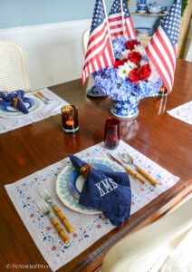 A red, white, and blue floral tablescape for Independence Day. Set with Sarah Flint placemats, Wedgwood Queen's Ware, Mottahedeh blue lace, bamboo flatware, hydrangea, and flags.