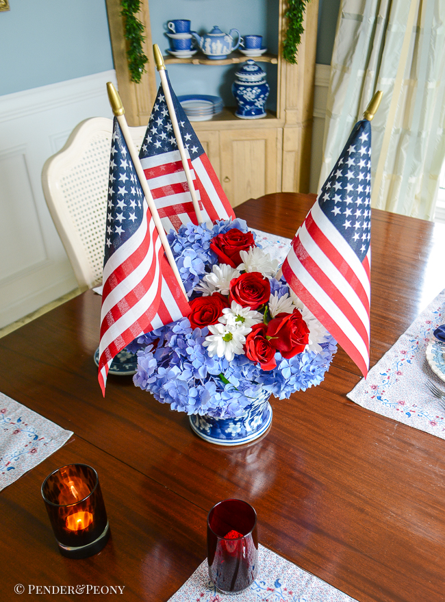 4th of July floral centerpiece with blue hydrangea, red roses, white daisies, and American flags in a blue and white Chinese temple jar.