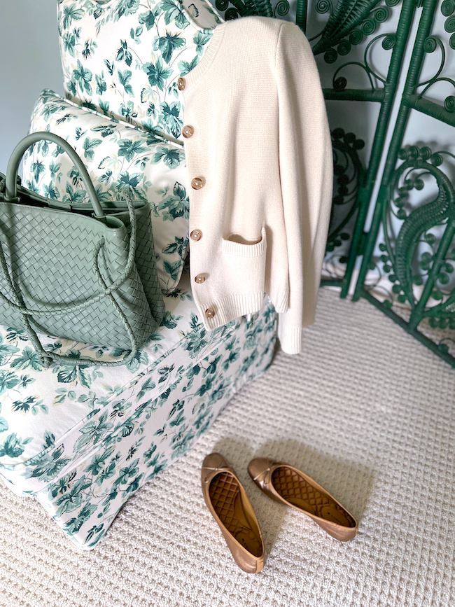Mongolian cashmere ivory cardigan draped on chair with gold ballet flats and sage green leather handbag