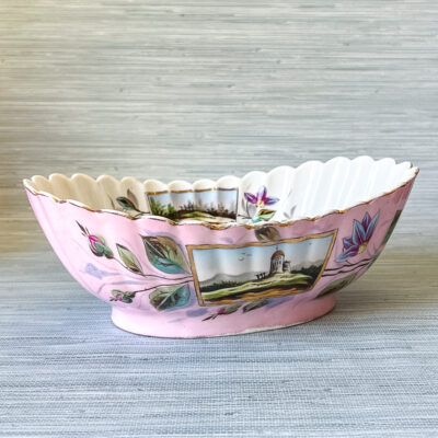 A unique bowl with fluted sides, landscape scenes, scrolling florals, and a vivid pink hue.