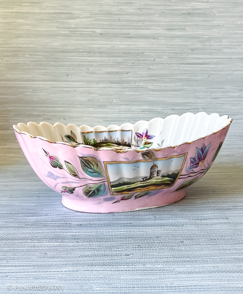 A unique bowl with fluted sides, landscape scenes, scrolling florals, and a vivid pink hue.
