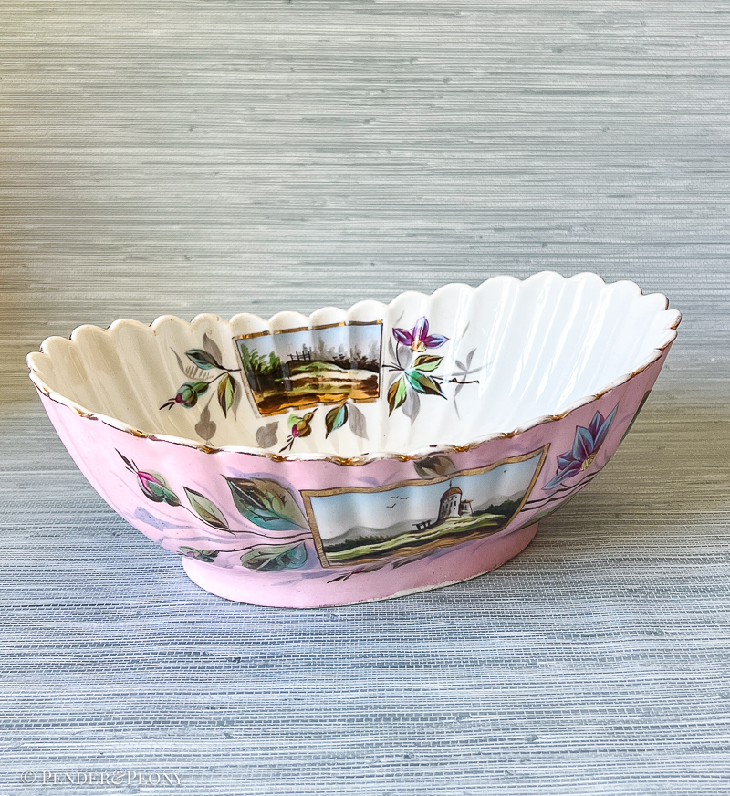 A unique bowl with fluted sides, landscape scenes, scrolling florals, and a vivid pink hue.