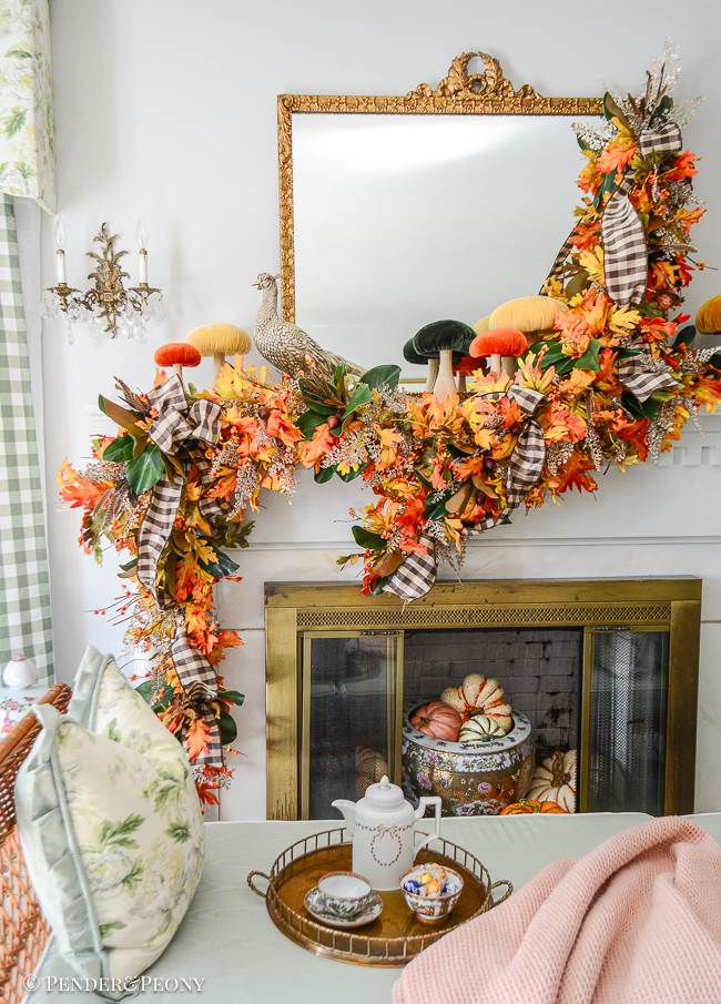 A fall mantel garland created with orange and gold oak leaves, bittersweet, magnolia, glittered fern, brown and white gingham ribbon. Mantel top decorated with velvet mushrooms and pheasant.