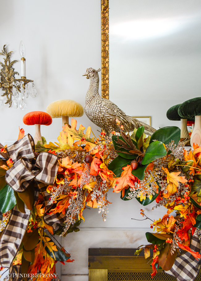 Glittered pheasant statue perches on mantel for autumn decor surrounded by velvet mushrooms and fall garland of oak, magnolia, bittersweet, and fern.
