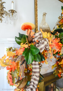A close up view of the fall mantel garland made from oak leaves, bittersweet, magnolia, brown and white gingham ribbon, and glittered fern