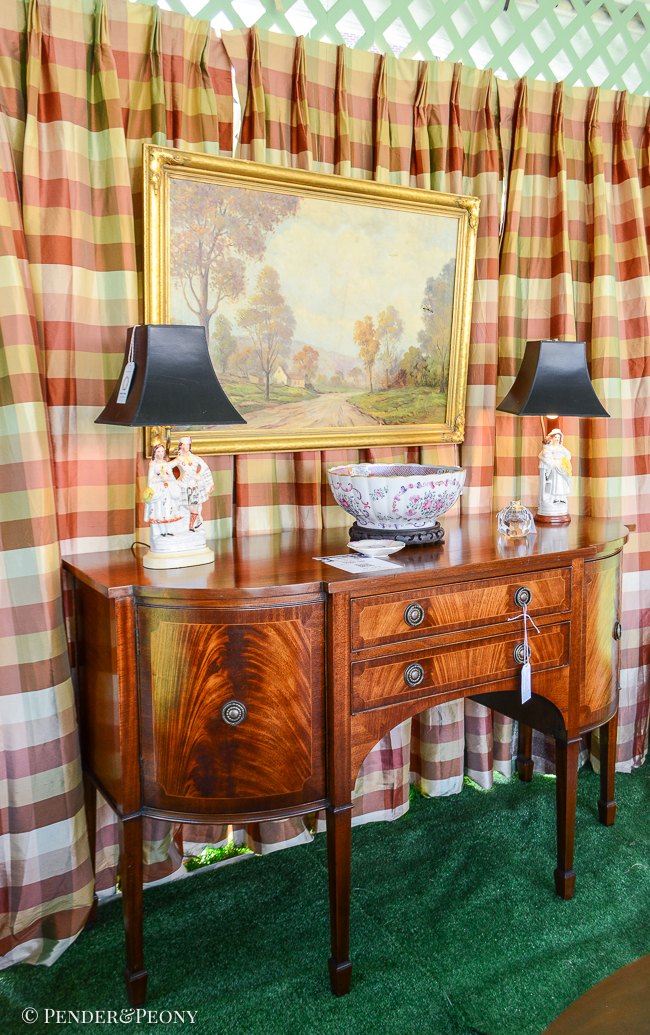 Back wall of design tent hung with silk plaid curtains in pink, burgundy, and green with English mahogany sideboard, landscape painting, and Staffordshire flatback lamps