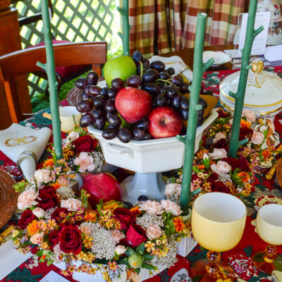 Thanksgiving centerpiece idea with ironstone compote filled with fruit surrounded by a surtout de table with flowers and stick candles