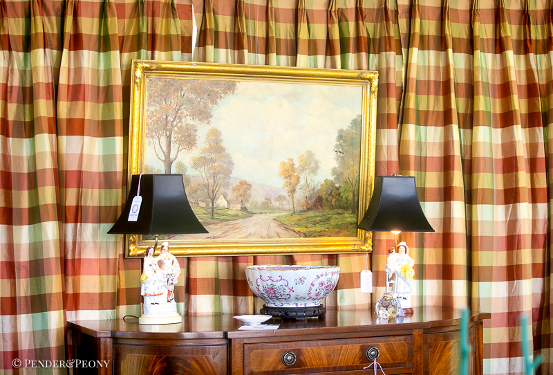 Back wall of design tent hung with silk plaid curtains in pink, burgundy, and green with English mahogany sideboard, landscape painting, and Staffordshire flatback lamps