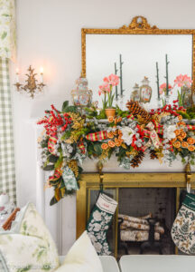 A Grand Botanical Christmas mantel decoration with DIY garland made of magnolia, pine, cedar, red berries, gold fern, orange slices, ribbon, and amaryllis.