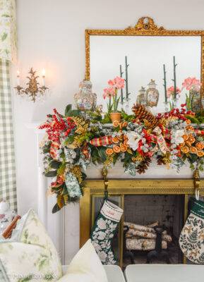 A Grand Botanical Christmas mantel decoration with DIY garland made of magnolia, pine, cedar, red berries, gold fern, orange slices, ribbon, and amaryllis.