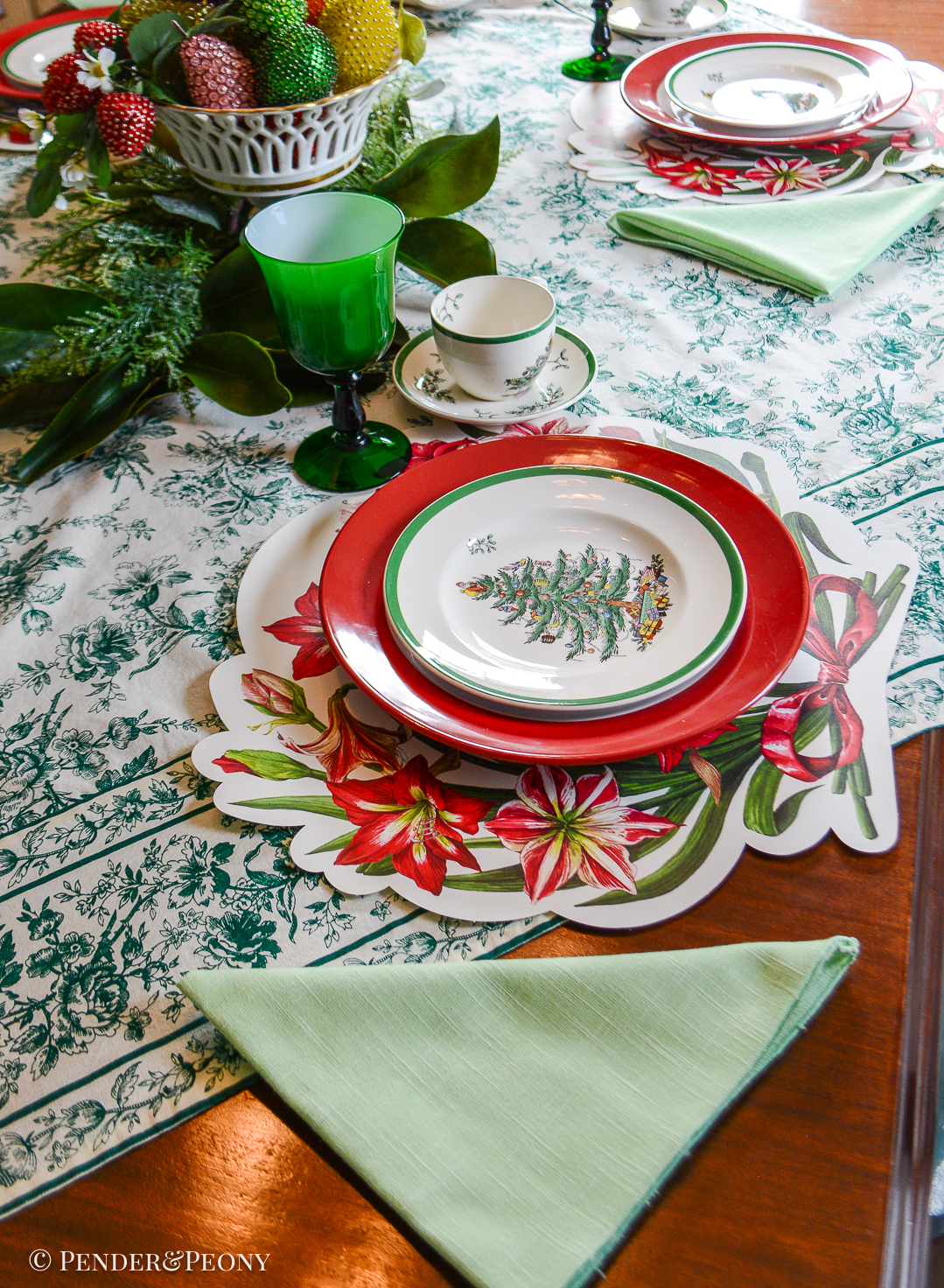 Green, white, and red Christmas table set with Spode's Christmas tree plates, amaryllis placemats from Hester & Cook, and vintage beaded fruit