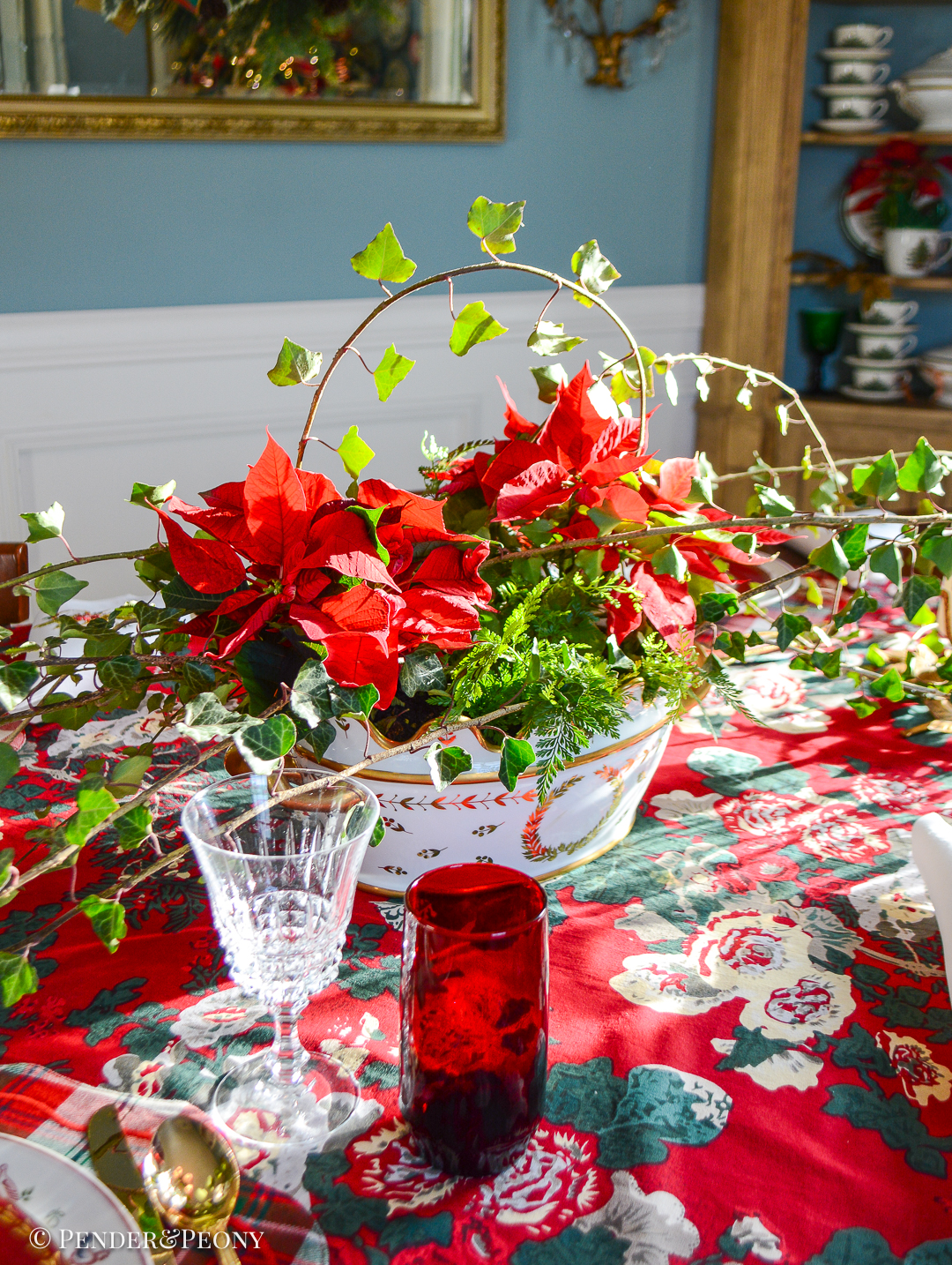 The Christmas table centerpiece with red poinsettia, fern, and ivy in a gilt porcelain cachepot