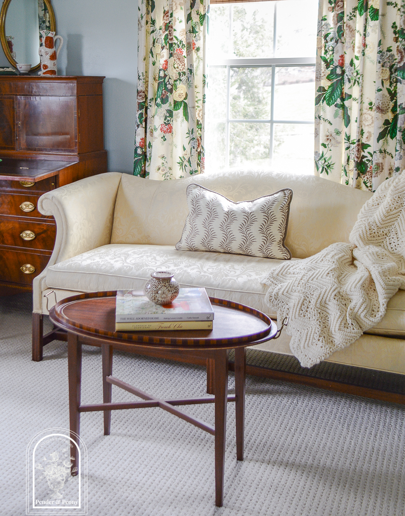 Ivory damask camel back sofa with tray top table, crochet afgan, and scrolling fern pillow in master bedroom