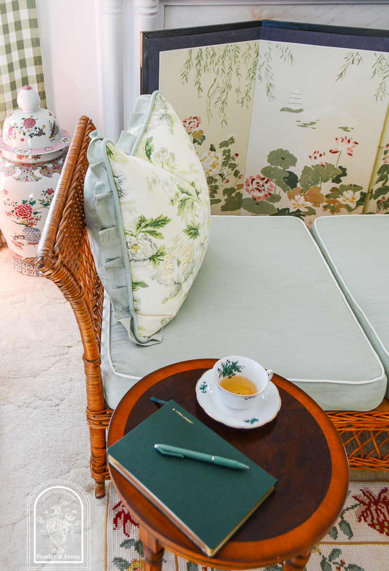 Wicker daybed with chintz pillow and side table with china teacup and green leather note book - cultivate beauty in your home with just a few small efforts