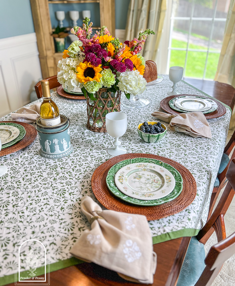 A green and white summer table with Royal Doulton china, cabbageware, linen napkins, Indian block print tablecloth, white opaline goblets, and sunflowers