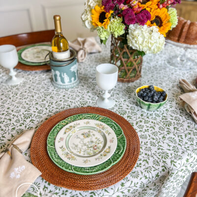 A green and white summer table with Royal Doulton china, cabbageware, linen napkins, Indian block print tablecloth, white Portieux Vallerysthal goblets, and sunflowers