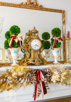 A gold maple leaf garland for fall mantel decor decorated with brown, pink, and burgundy ribbons
